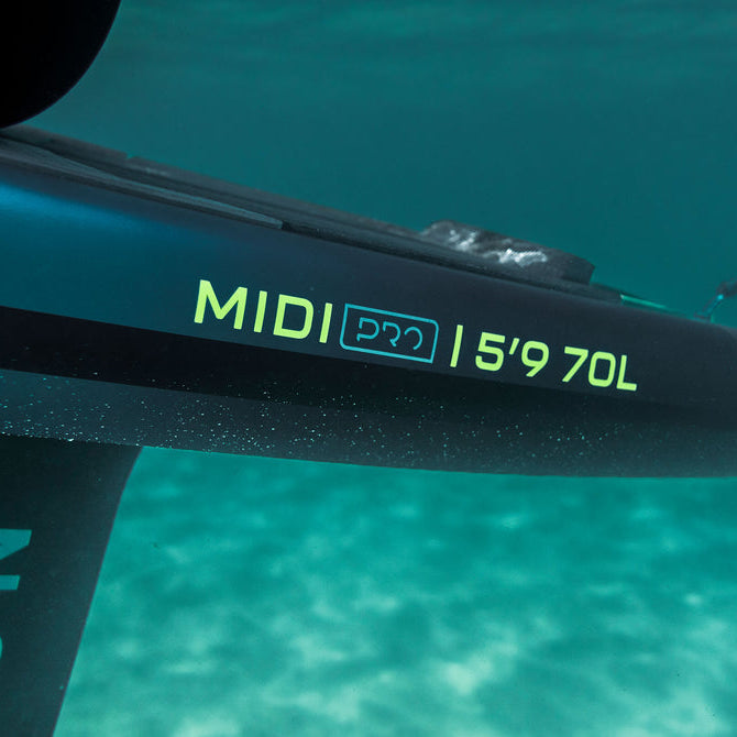 Close-up underwater shot of a black hydrofoil board with neon green branding reading 'MIDI PRO | 5'9 70L' and part of the 'NORD' brand name visible on the vertical stabilizer, set against turquoise ocean water.